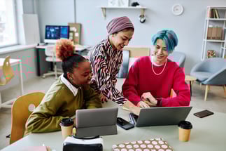 young creative gen z employees gather around laptops and tablets in workplace